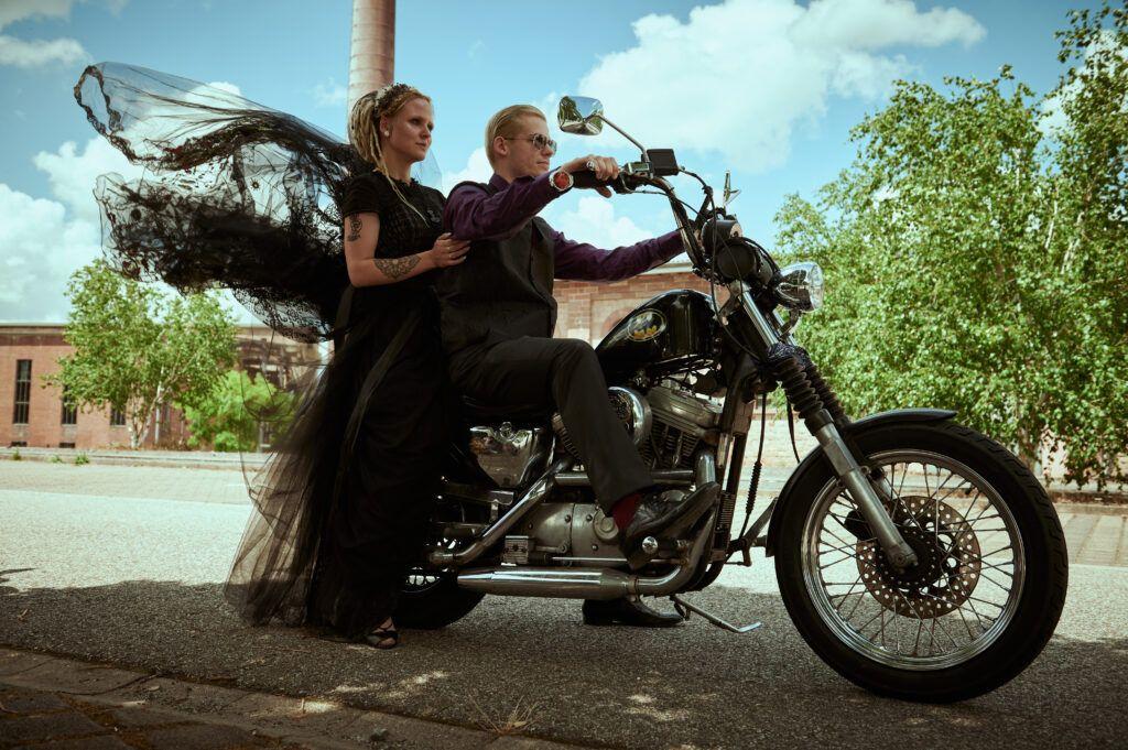 Ein Brautpaar zusammen auf einem Motorrad von Harley-Davidson, beide ganz in schwarz gekleidet.